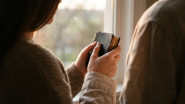 Gün batımında pencere önünde dua kitabını göğsüne bastıran eller