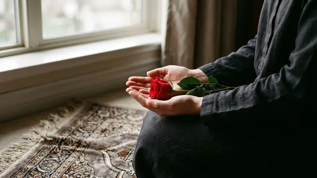 Pencere önünde seccadede elinde kırmızı gülle dua eden kadın