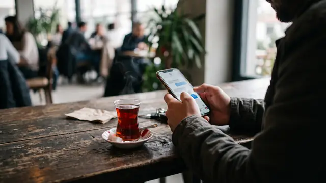 Kafe masasında çay yanında telefondan mesaj okuyan kişi