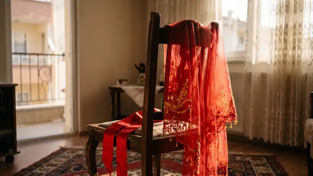 Güneşli odada ahşap sandalyede asılı kırmızı gelin duvağı