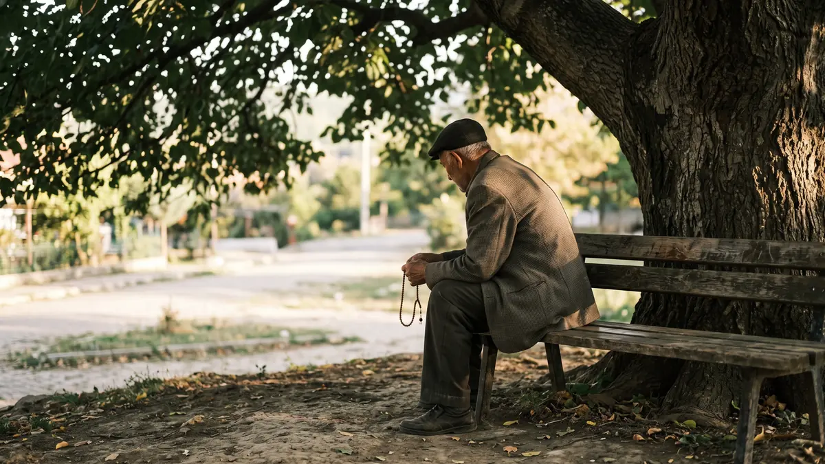 Ağaç altında bankta elinde tesbihle sabırla oturan yaşlı adam