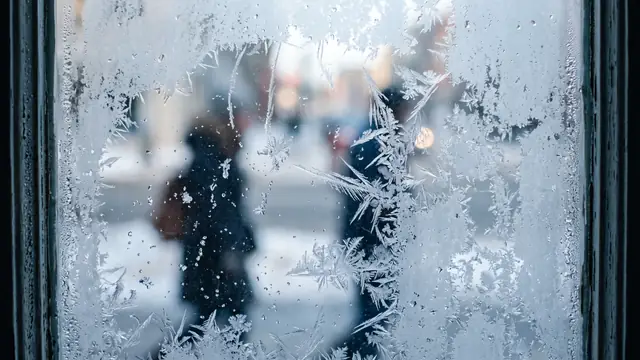 Buz kristalleriyle kaplı pencere camı ve dışarıda bulanık figürler