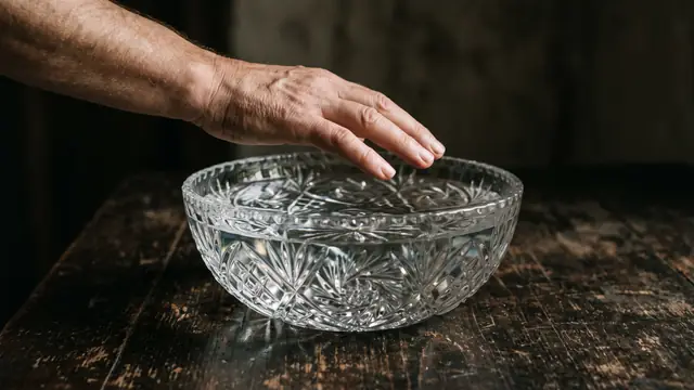 Karanlık arka planda ışık yansıyan kristal su kasesi ve üzerindeki el