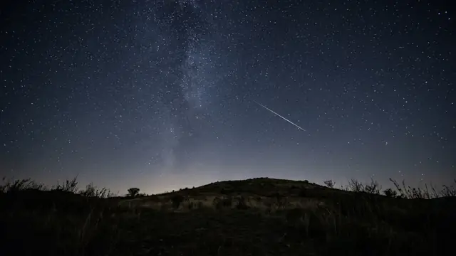 Karanlık tepe üzerinde yıldızlı gökyüzü ve kayan yıldız